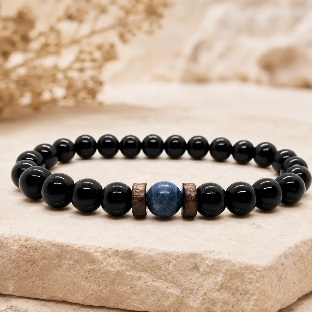 Obsidian lapis lazuli bracelet with polished black obsidian beads, natural blue lapis lazuli centerpiece, and wood spacers on a stone display.