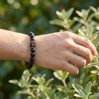Hand wearing a black beaded bracelet with a blurred green foliage background