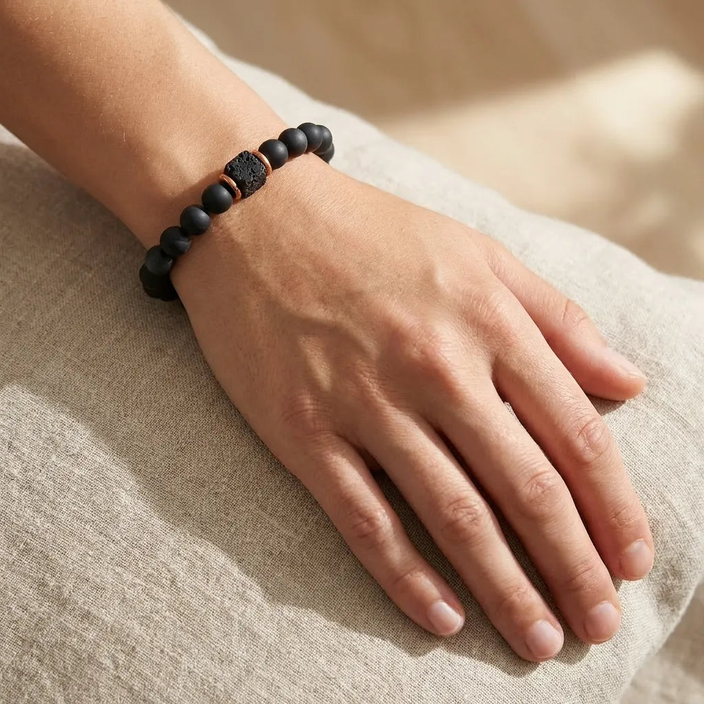 Hand wearing a black beaded bracelet on a beige fabric background