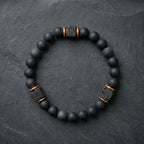Black onyx lava bracelet with metallic accents on a dark stone background