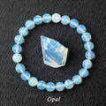 Opal bracelet with soft blue-white opalescent beads surrounding a raw pale opalite specimen on dark background