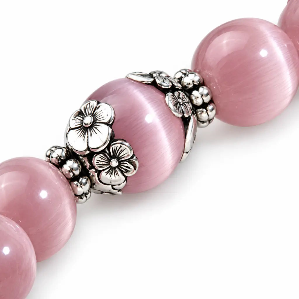 Pink Catseye bracelet close-up with luminous pink beads, silver filigree setting and floral charm for refined detail.