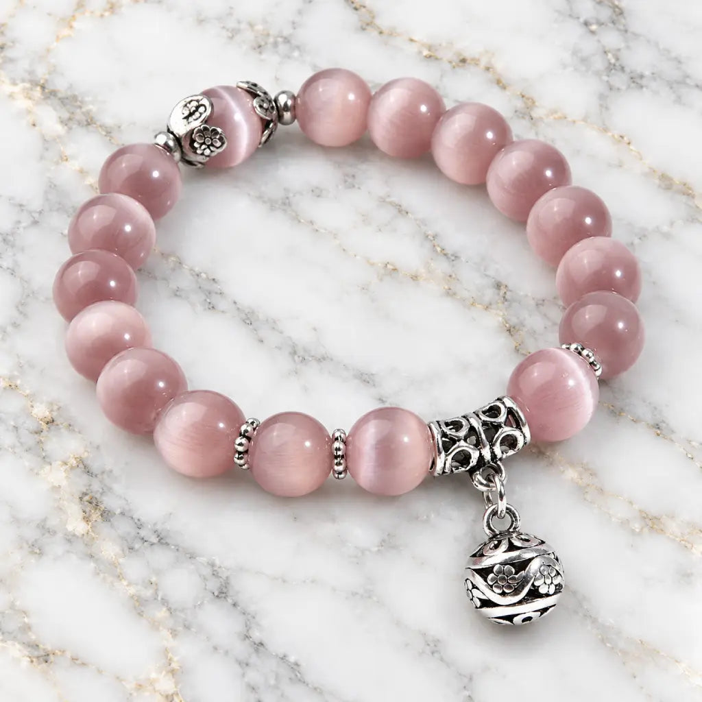 Pink Catseye bracelet with glossy pink beads, silver floral accents and a dangling charm for an elegant feminine look.
