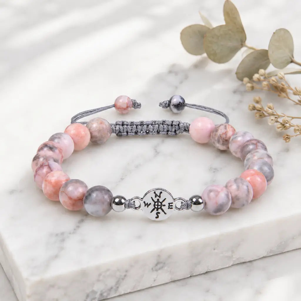 Pink Zebra Jasper stone bracelet displayed on white marble with natural botanical accents for modern elegance