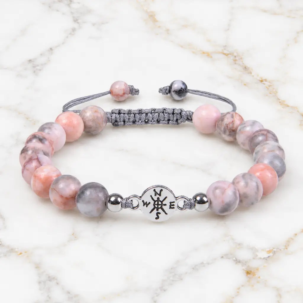 Pink Zebra Jasper bracelet with polished gemstone beads and silver charm on marble background for elegant healing style