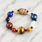 Planet bead tiger eye bracelet arranged on a premium marble surface with polished natural gemstone beads, tiger eye, quartz, and striped agate centerpiece.