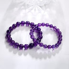 Two purple glass bead bracelets in different sizes, arranged on white fabric to compare polished round beads and stretch construction in one clean bright product view side by side.