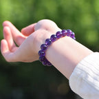 Purple glass bead bracelet worn on a wrist outdoors, showing polished translucent round beads and simple stretch construction in natural light for a clear view of color and finish.
