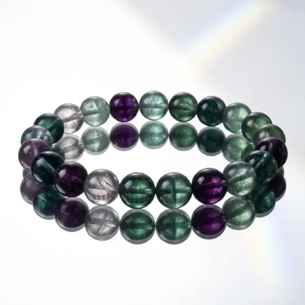 Rainbow Fluorite Crystal Bracelet on white reflective surface, clean product shot highlighting bead clarity and premium polished finish