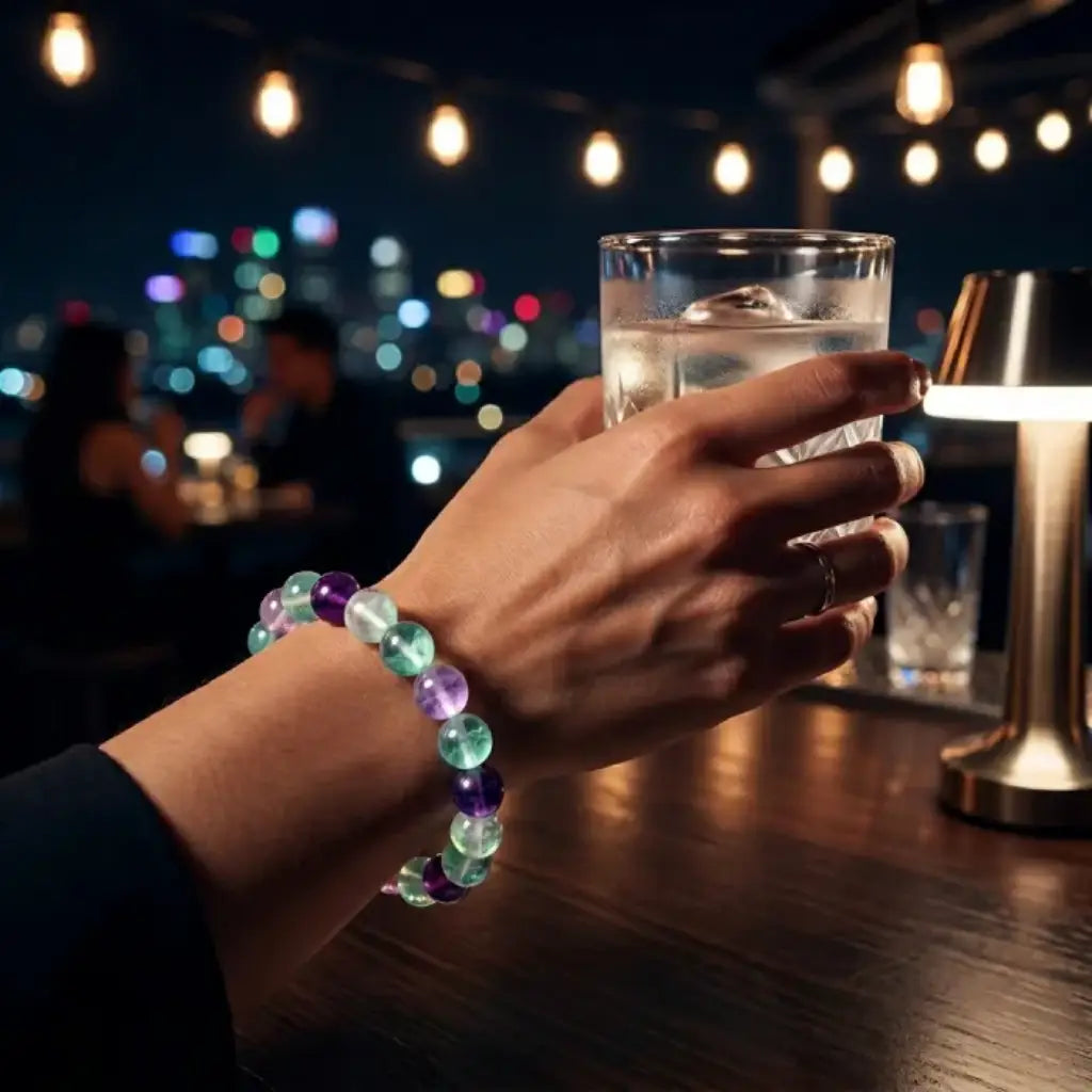 Rainbow Fluorite Crystal Bracelet worn at night holding glass, glowing beads highlight stylish energy confidence in modern lifestyle