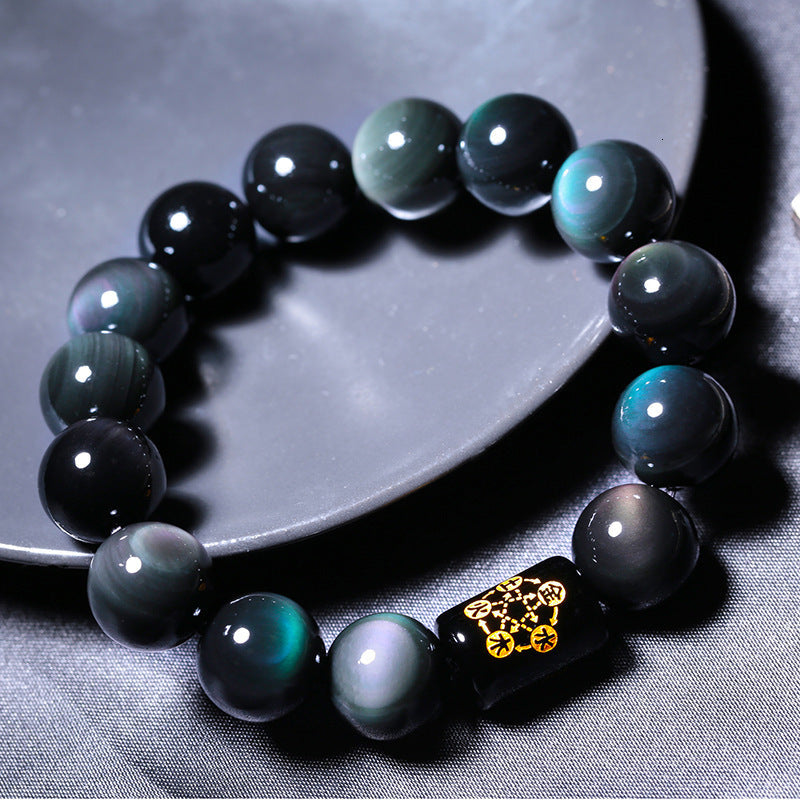 Rainbow obsidian bracelet in a detailed circular flat lay, showing polished black beads with green, blue, and purple sheen, plus a black barrel accent with decorative gold symbols.
