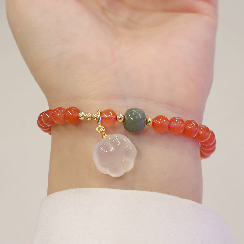 Red agate bracelet worn around the wrist, featuring translucent orange-red beads, one green accent bead, gold-tone spacers, and a white cat-paw charm in a full clear close-up view.