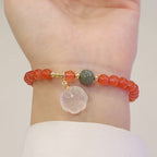 Red agate bracelet worn around the wrist, featuring translucent orange-red beads, one green accent bead, gold-tone spacers, and a white cat-paw charm in a full clear close-up view.