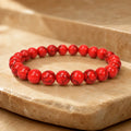 Red howlite bracelet with polished gemstone beads on a natural stone display for stylish healing energy wear