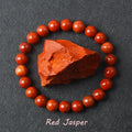 Red Jasper bracelet with deep brick-red polished beads surrounding a raw Red Jasper specimen on dark background