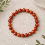 Red jasper stone bracelet glossy red bead stretch bracelet on stone surface, energizing crystal jewelry daily wear