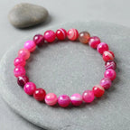 Rose Stripe Agate bracelet polished pink banded beads on stone tray, calming crystal accessory for mindfulness