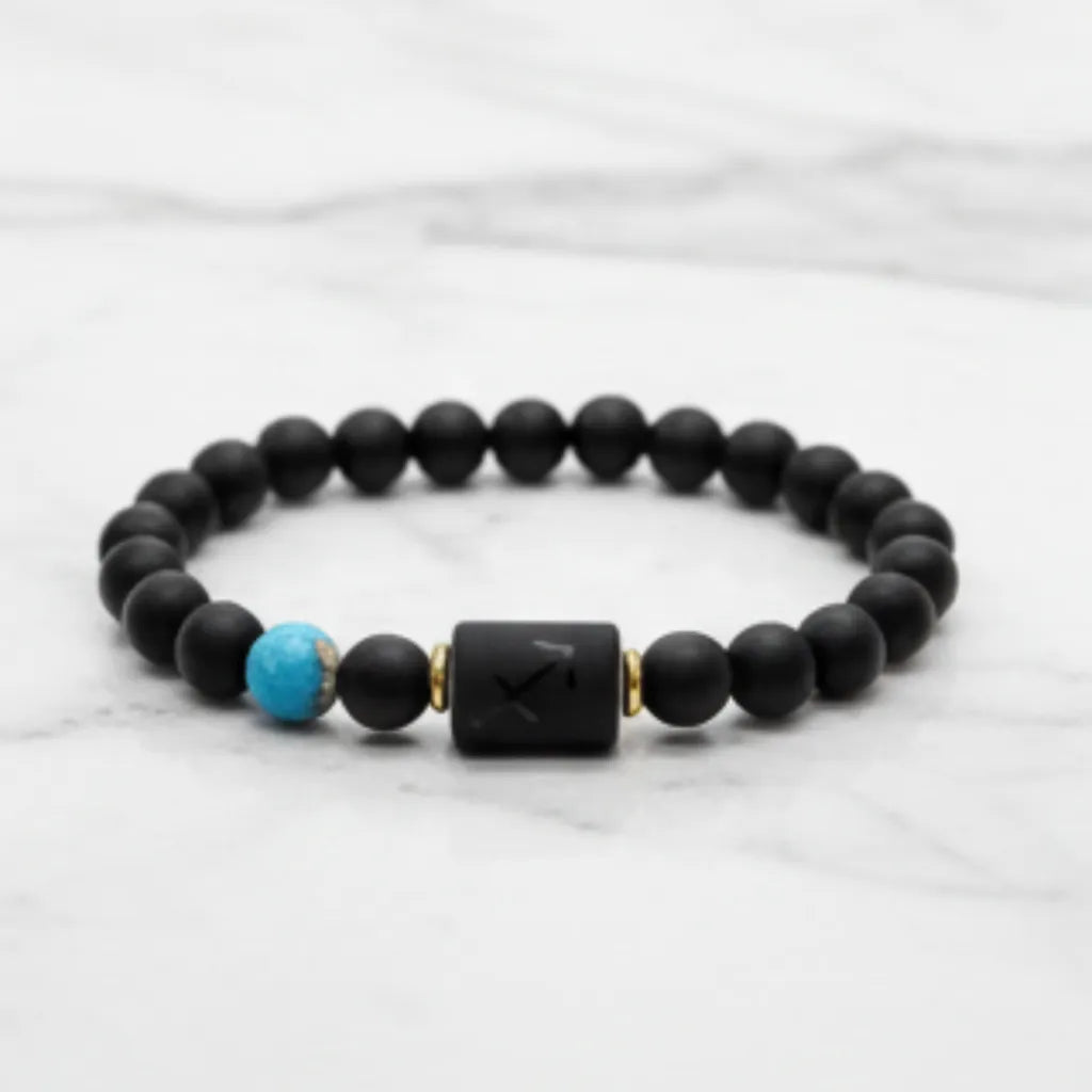 Sagittarius zodiac bracelet with matte black beads, turquoise accent bead and engraved center charm on marble background