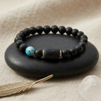 Black sagittarius zodiac bracelet with a turquoise bead on a dark stone surface, with a feather and shell in the background.