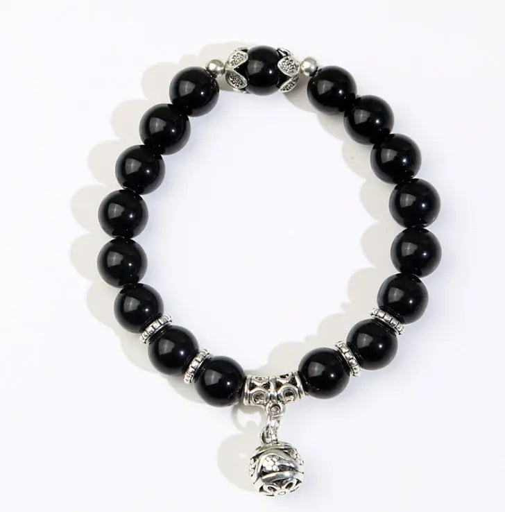 A beaded stretch bracelet featuring glossy black round beads, silver-toned spacer beads, and a dangling silver bell charm, displayed on a clean white background.