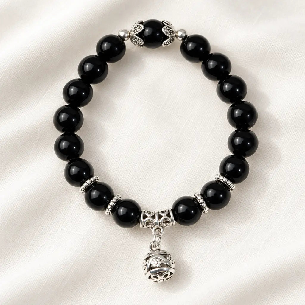 Shadow guardian obsidian bracelet with sleek black beads and ornate silver charm, presented on soft fabric for timeless elegance.