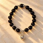 Shadow guardian obsidian bracelet with polished black beads and ornate silver charm, displayed in warm light for bold style.