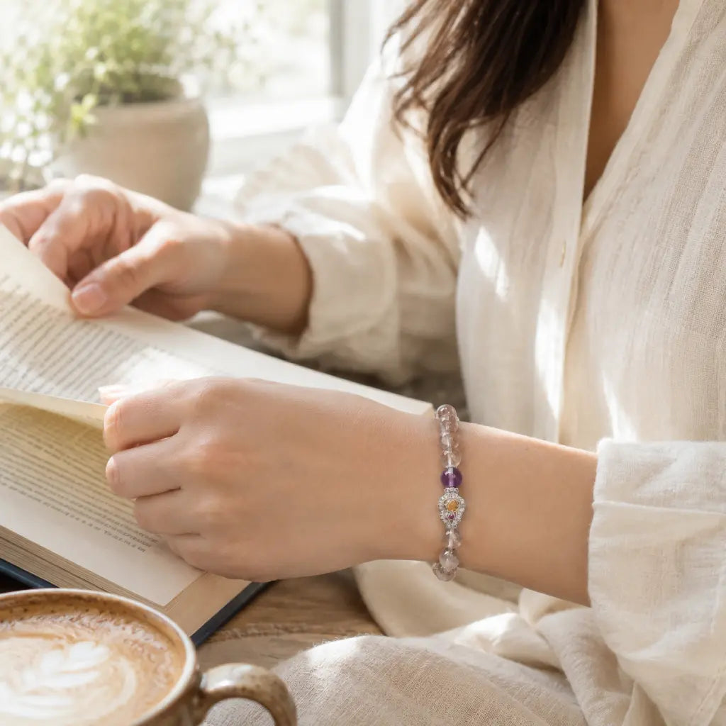 Person reading a book with a cup of coffee and a bracelet on a light background