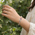 Hand wearing a beaded bracelet with greenery in the background