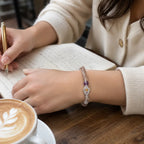 Person writing in a notebook with a cup of coffee on a wooden table