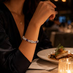 Person wearing a bracelet with a plate of food and candlelight in the background