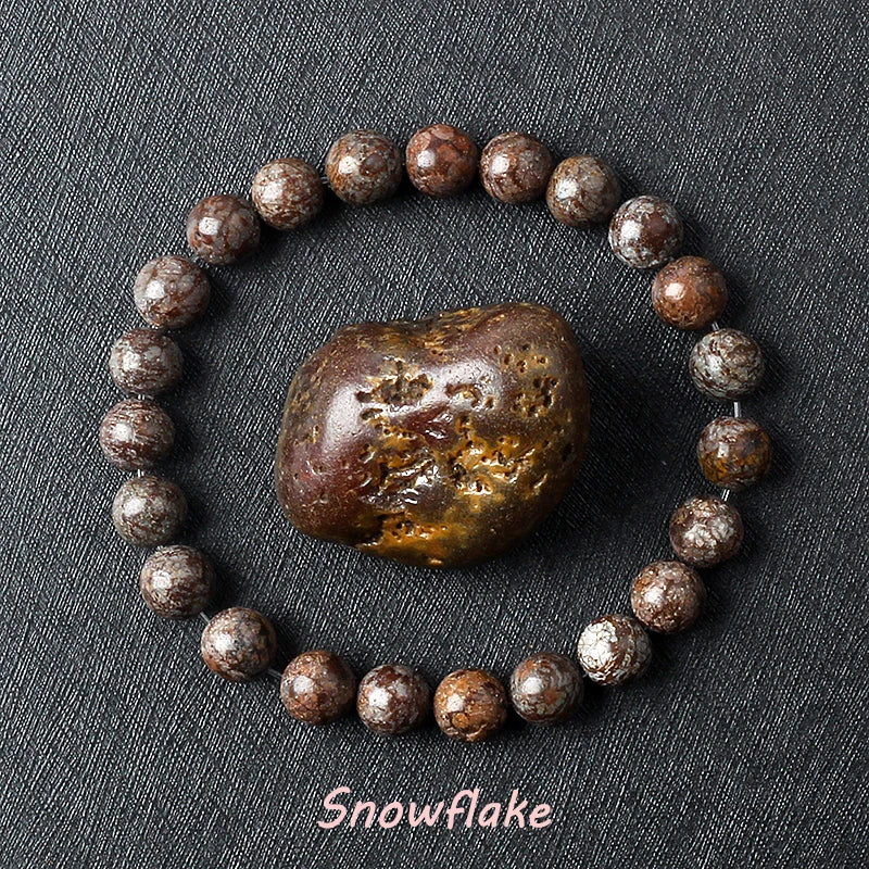 Snowflake Obsidian bracelet with dark brown beads and white crystal patterns surrounding a raw obsidian specimen on dark background