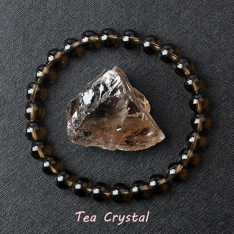 Tea Crystal bracelet with round smoky brown beads beside a raw matching crystal stone on dark fabric