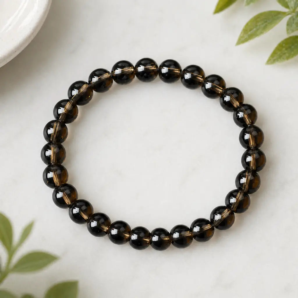 Tea crystal bracelet smoky brown bead stretch bracelet on marble with green leaves, elegant grounding jewelry style