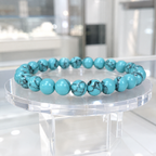 Teal howlite bracelet featuring polished gemstone beads on a clear stand for refined crystal style wear