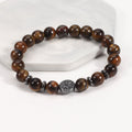 Tiger eye bracelet with glossy golden-brown 8 mm round beads, four dark spacer rings, and a round tree-design focal bead, displayed at a clear angle on a white stone display stand.