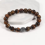 Tiger eye bracelet with glossy golden-brown 8 mm round beads, four dark spacer rings, and a round tree-design focal bead, displayed at a clear angle on a white stone display stand.