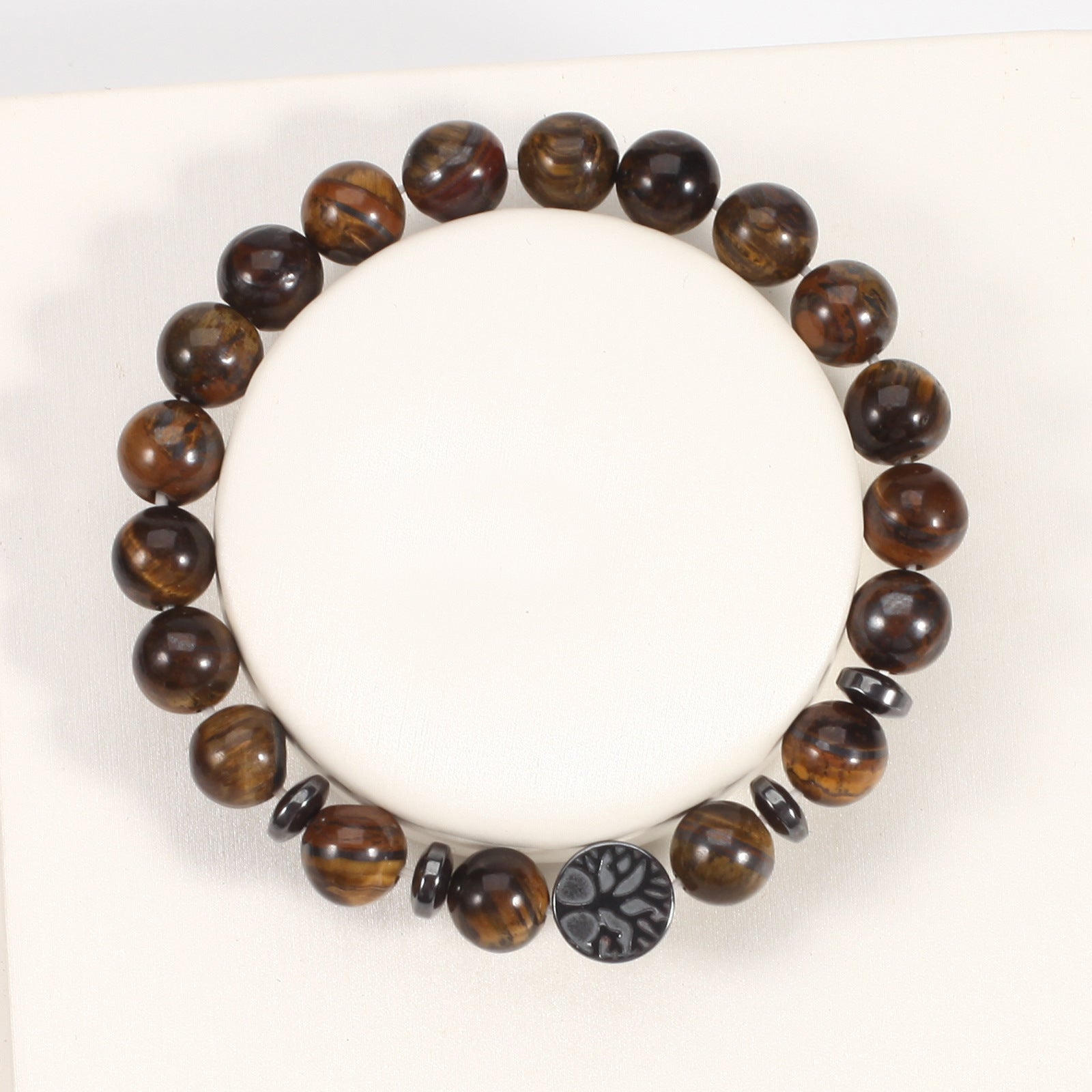 Tiger eye bracelet with glossy brown gold 8mm round beads, four dark spacer rings, and a round tree-design focal bead, seen from above on a white jewelry display form in full view.