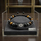 Beaded bracelet with a compass charm on a gray stand inside a clear display case, with 'Quiet Moon Beads' branding.