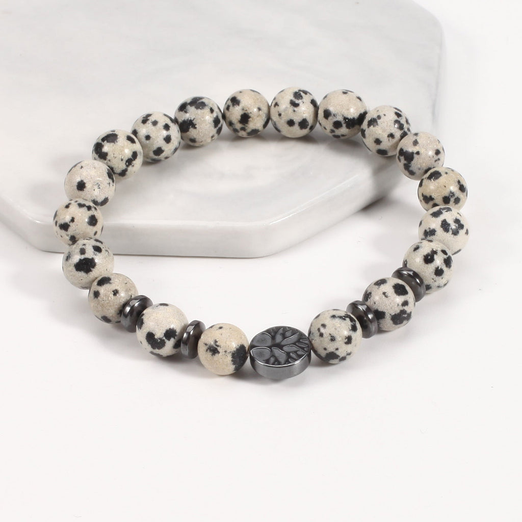 Tree of life stone bracelet in the Spotted Stone option, with cream and black-spotted 8mm beads, black spacer rings, and a round dark tree-design focal bead in bright studio light.