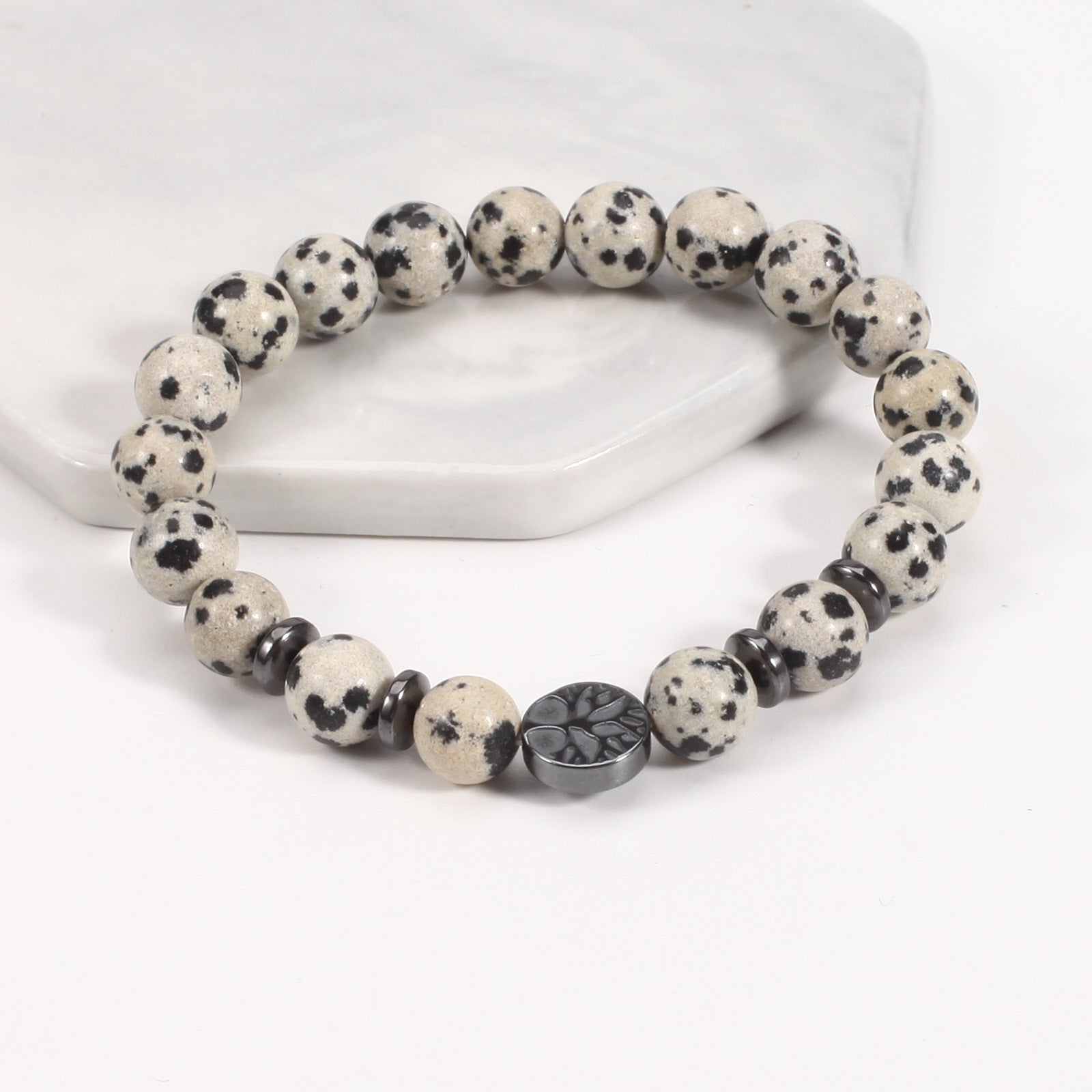 Tree of life stone bracelet in the Spotted Stone option, with cream and black-spotted 8mm beads, black spacer rings, and a round dark tree-design focal bead in bright studio light.