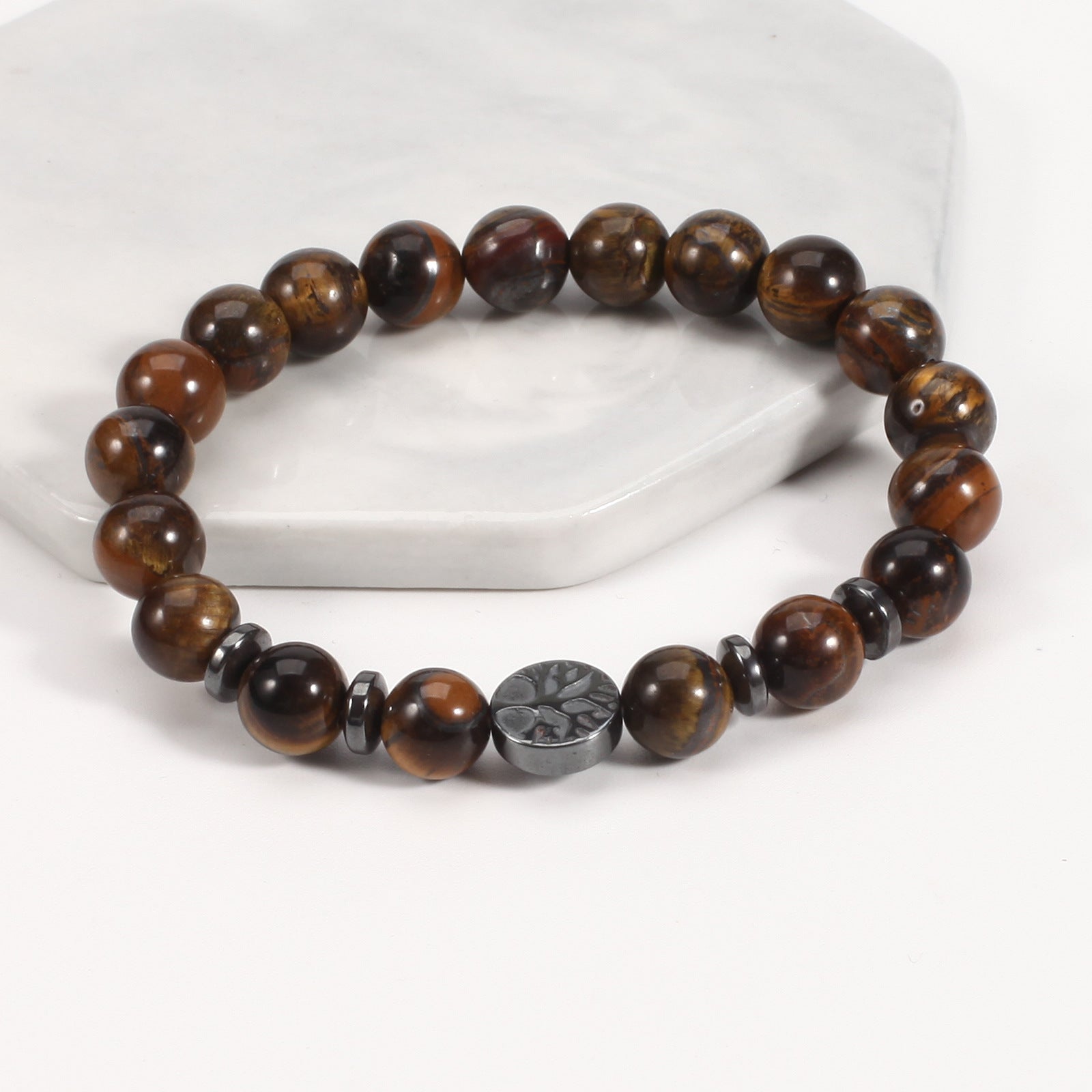 Tree of life stone bracelet with glossy golden tiger eye 8 mm beads, black spacer rings, and a round dark tree-design focal bead, displayed at a clear angle on a white stone stand.