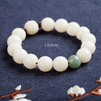 White bodhi seed bracelet close-up marked 10 mm, showing smooth round ivory-color beads, one green accent bead, dark spacers, and a carved white lotus-style focal bead in view now.