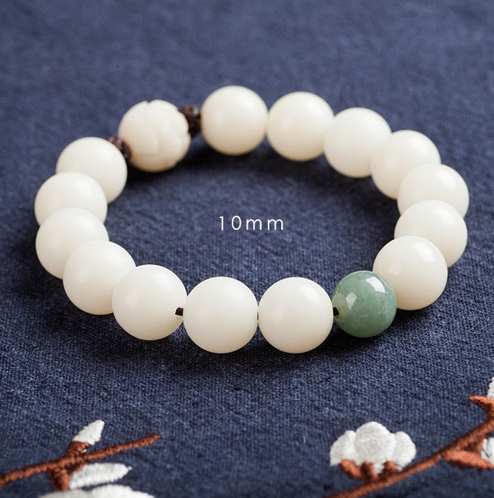 White bodhi seed bracelet close-up marked 10 mm, showing smooth round ivory-color beads, one green accent bead, dark spacers, and a carved white lotus-style focal bead in view now.