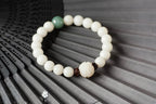 White bodhi seed bracelet arranged on dark bamboo slats with cream round beads, one green accent bead, dark carved spacers, and a larger white lotus style focal bead in fair light.