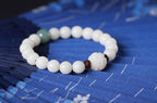 White bodhi seed bracelet on blue patterned fabric with smooth ivory-color beads, one green accent bead, two dark spacers, and a carved white lotus-style focal bead in fuller view.