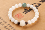 White bodhi seed bracelet on calligraphy paper with pale round beads, one green accent bead, two dark carved spacers, and a larger carved white lotus-style focal bead in low light.