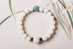 White bodhi seed bracelet displayed flat with smooth round ivory-color beads, one green accent bead, two dark carved spacers, and a larger carved white lotus-style focal bead here.