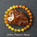 Yellow Popcorn Agate stone surrounded by yellow and orange beads on a dark fabric background
