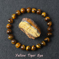 Yellow Tiger Eye bracelet with golden brown chatoyant beads surrounding a raw tiger eye specimen on dark background