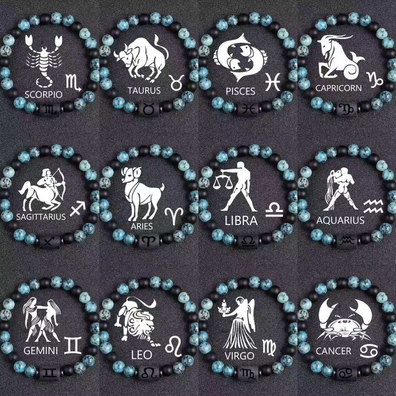 Zodiac bracelet collection with all twelve signs, blue-green jasper, matte black onyx, hematite spacers, and black zodiac centerpieces, shown in a full product view on dark fabric.